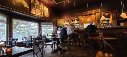 Cozy café interior with patrons at the bar, large windows, and warm lighting creating a welcoming atmosphere.