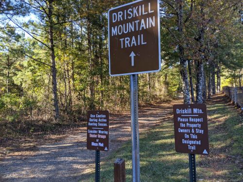 Signage for Driskill Mountain Trail, with warnings about caution and respect for property owners, surrounded by trees.