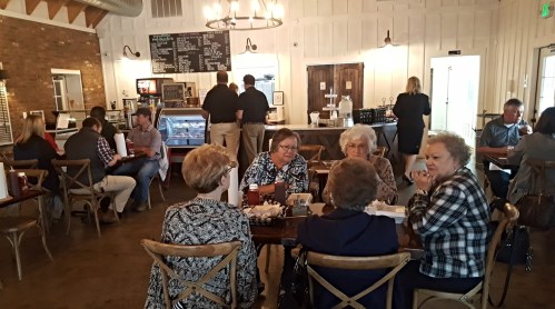 A cozy café scene with groups of people chatting at tables, a counter in the background, and a warm, inviting atmosphere.