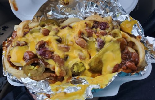 A close-up of a loaded taco with beans, jalapeños, and melted cheese, served in foil.