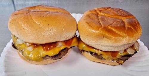 Two cheeseburgers with melted cheese, onions, and sauce on toasted buns, served on a white paper plate.