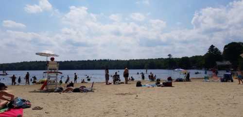 A sunny beach scene with people swimming, lounging on sand, and enjoying the water under a blue sky with clouds.