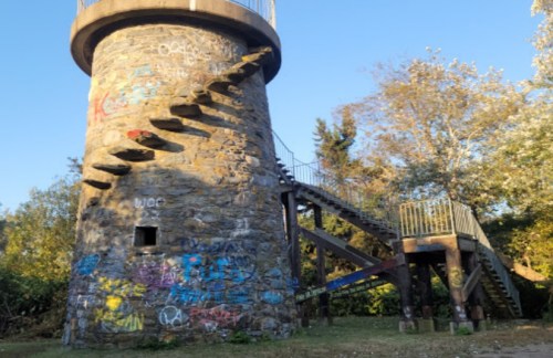 A stone tower with a spiral staircase, surrounded by trees and covered in colorful graffiti.