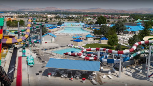 Aerial view of a water park featuring colorful slides, pools, and lounge areas surrounded by trees and mountains.