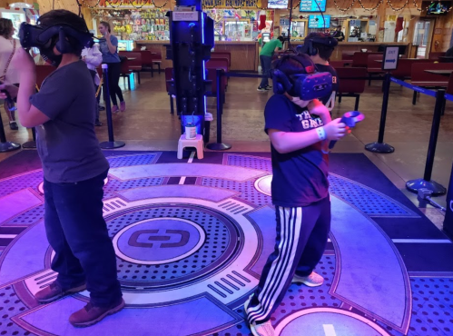 Two children wearing VR headsets stand on a colorful gaming platform, engaged in a virtual reality experience.