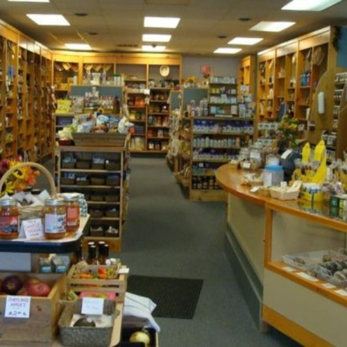 A cozy store interior filled with shelves of various food products and goods, featuring wooden displays and a welcoming atmosphere.