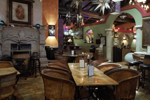 Cozy restaurant interior with wooden tables, chairs, and a fireplace, featuring warm lighting and decorative elements.