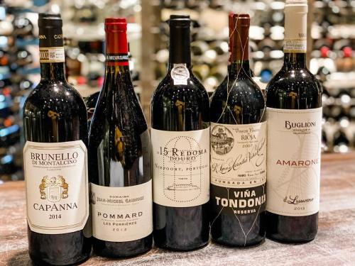 Five wine bottles displayed on a wooden surface, featuring labels from Brunello, Pommard, Rioja, and Amarone.
