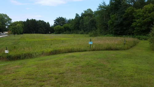 A grassy field with trees in the background and signs marking different areas. Clear blue sky above.