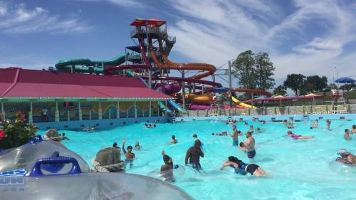 A busy water park with colorful slides, a wave pool, and people enjoying the sun and water activities.