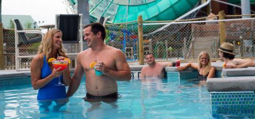 A couple enjoys colorful cocktails in a pool, surrounded by friends relaxing and having fun at a water park.