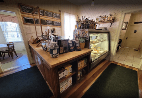 Cozy café interior featuring a wooden counter, display case with pastries, and shelves of drinks and snacks.