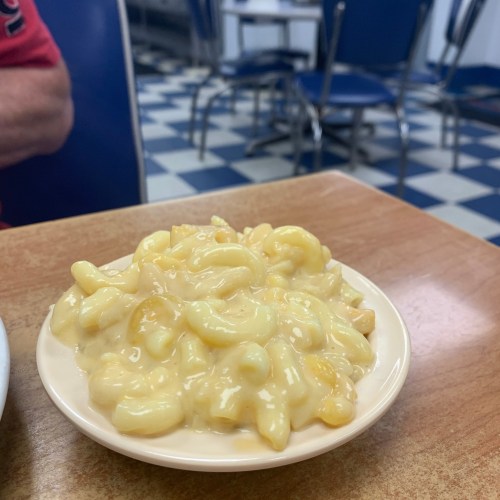 A small dish of creamy macaroni and cheese on a wooden table in a diner setting.