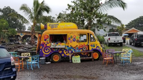 A colorful ice cream truck parked in a rainy outdoor setting with tables and chairs nearby.