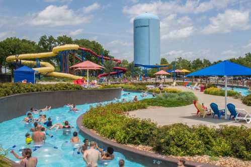 A water park scene with slides, a lazy river, and people enjoying the sun under colorful umbrellas.