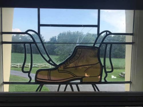 Stained glass window featuring a boot design with a green landscape visible outside.