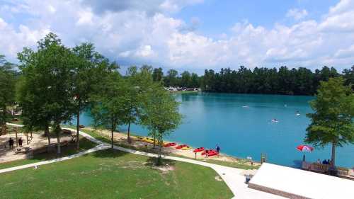 A serene lake surrounded by trees, with kayaks on the water and people enjoying the outdoors under a cloudy sky.