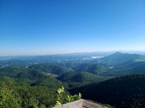 A panoramic view of lush green mountains under a clear blue sky, with valleys and distant peaks visible.