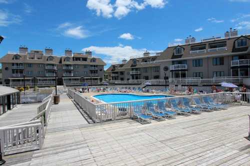 A sunny pool area surrounded by buildings, with lounge chairs and people enjoying the water on a clear day.