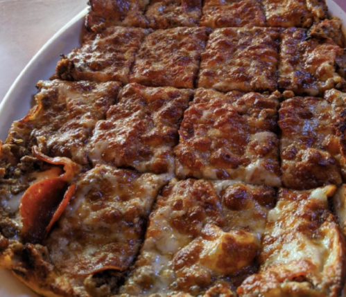 A close-up of a rectangular pizza topped with melted cheese, pepperoni, and a golden-brown crust, sliced into squares.