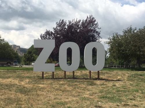 Large white letters spelling "ZOO" on a grassy area with trees and a cloudy sky in the background.