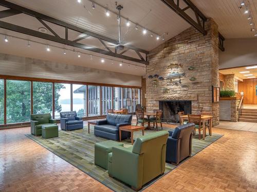 Cozy lounge area with seating, a stone fireplace, and large windows overlooking a scenic view.