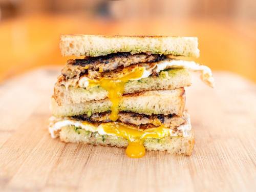 A stacked sandwich with crispy layers, featuring a runny egg, meat patty, and toasted bread on a wooden surface.