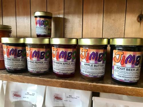 A shelf displaying various jars of colorful jams and jellies, labeled with "Jimbo" and different flavors.
