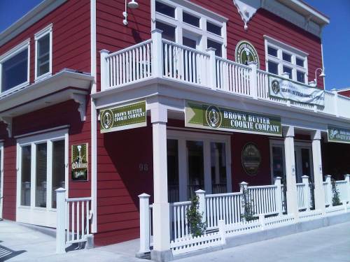 Exterior of a red building with white trim, featuring signs for Brown Butter Cookie Company and a welcoming porch.
