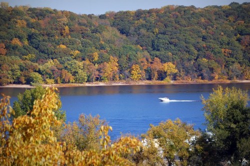 A boat glides across a calm lake surrounded by vibrant autumn foliage.