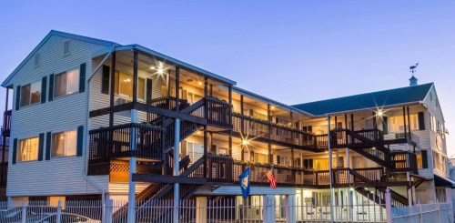 A multi-story building with balconies, illuminated at dusk, featuring a staircase and flags outside.