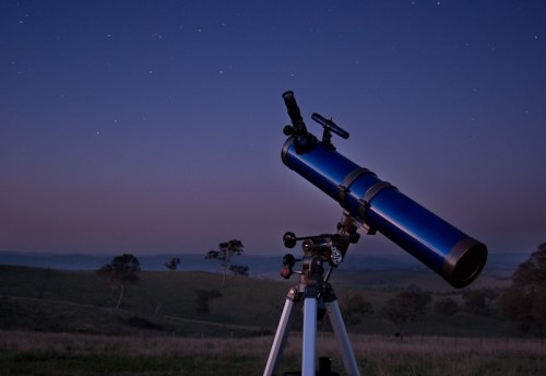 A blue telescope on a tripod, set against a starry night sky and distant hills.