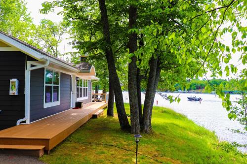 A cozy lakeside cabin surrounded by trees, with a wooden deck and boats on the water in the background.