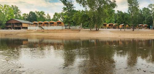 A serene riverside view featuring wooden cabins and lush greenery along the water's edge.
