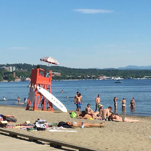 A sunny beach scene with a lifeguard tower, people swimming, and sunbathers on the sand.