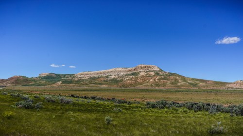 A wide landscape featuring rolling green hills and a prominent rocky plateau under a clear blue sky.