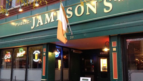 Exterior of Jamison's pub, featuring green signage, an Irish flag, and neon lights in a lively urban setting.