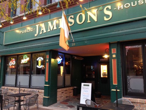 Exterior of Jamison's pub with an Irish flag, neon signs, and outdoor seating. Warm evening ambiance.