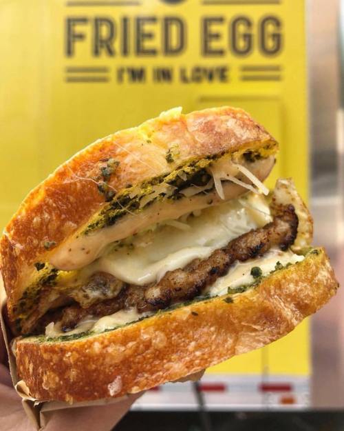 A close-up of a delicious sandwich with a fried egg, cheese, and meat, set against a bright yellow food truck background.