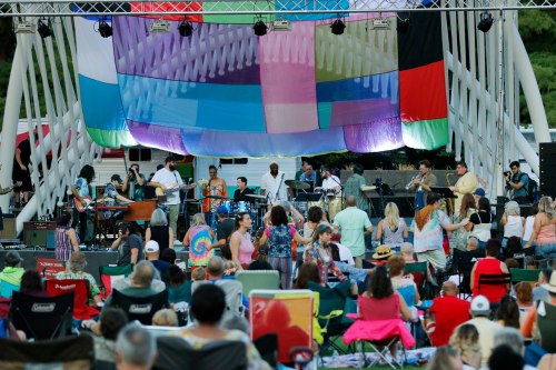 A lively outdoor concert scene with a band performing on stage and an audience enjoying the music. Colorful backdrop.