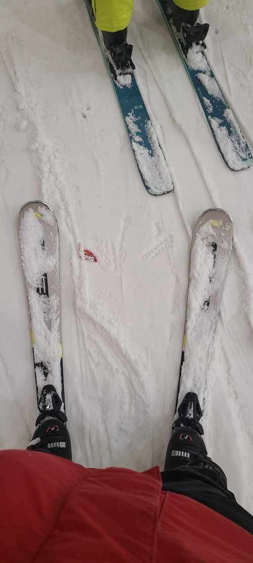 Two pairs of skis on snowy terrain, with one skier wearing a red jacket and the other in bright yellow gear.