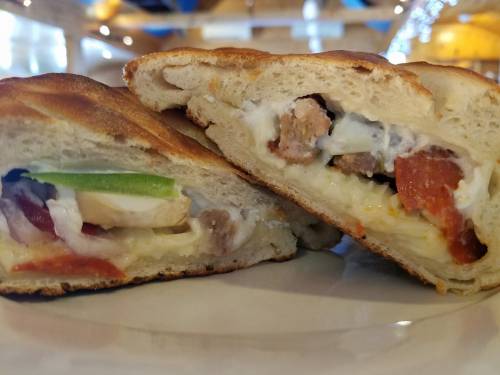 Close-up of a sliced calzone, revealing layers of cheese, vegetables, and meat inside a golden-brown crust.