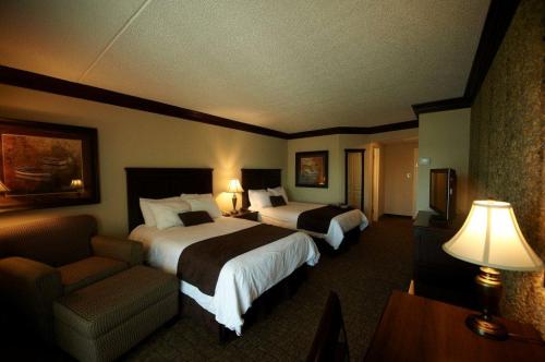 A cozy hotel room featuring two beds, a seating area, a desk, and warm lighting.