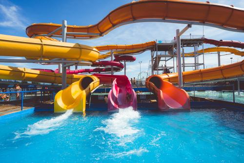 Colorful water slides twist above a bright blue pool, with people enjoying the water on a sunny day.