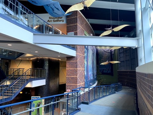 Interior view of a modern building featuring a staircase, art gallery sign, and hanging decorations.