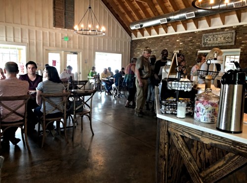 A bustling café interior with patrons dining, chatting, and a coffee station in the foreground. Warm, inviting atmosphere.