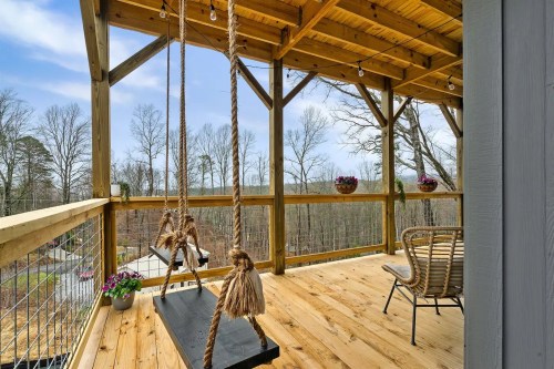 A wooden deck with swings, potted flowers, and a view of trees under a blue sky.