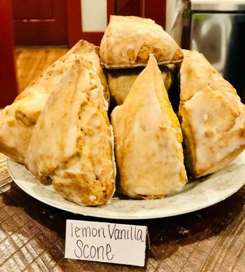 A plate of lemon vanilla scones, drizzled with icing, arranged in a pyramid shape with a label in front.