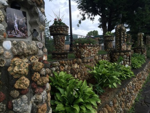 A decorative stone wall adorned with shells and plants, featuring flower pots and a photo in a frame.
