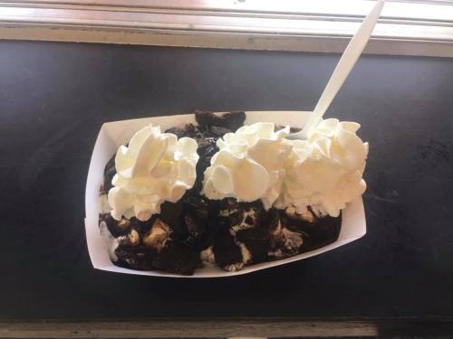 A dessert dish with crushed Oreos, chocolate sauce, and two dollops of whipped cream on top.